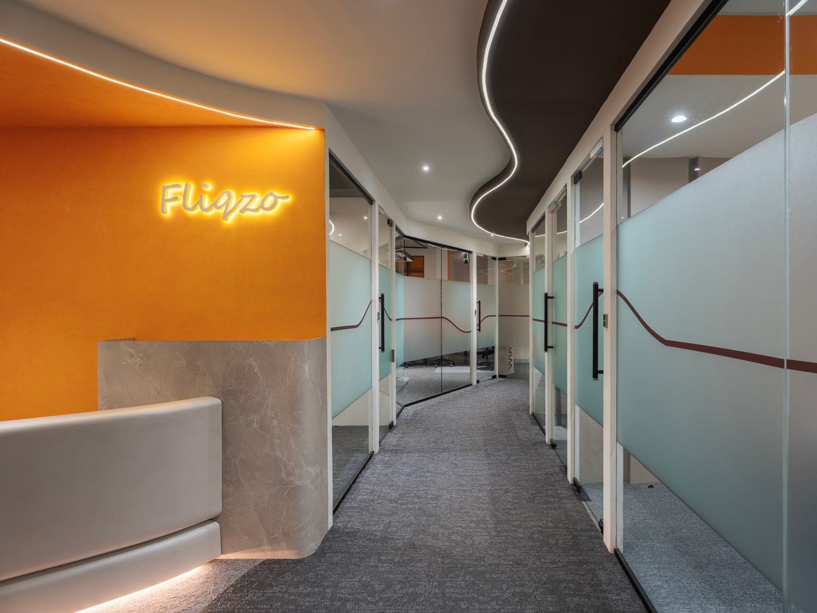 Curved corridor with frosted-glass cabin fronts and backlit Fliqzo sign at the Sungam Bypass Road office
